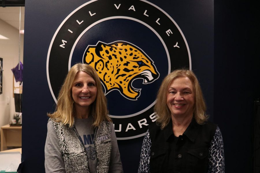 Next to each other, secretary Edie Waye and math teacher Laurie Deuschle stand in front of the jaguar in the office.