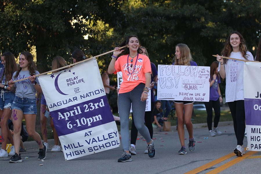 Smiling at the crowd, senior Maddy Williams leads the Relay for Life portion of the parade while holding a sign with sophomore Ellie Walker. 
