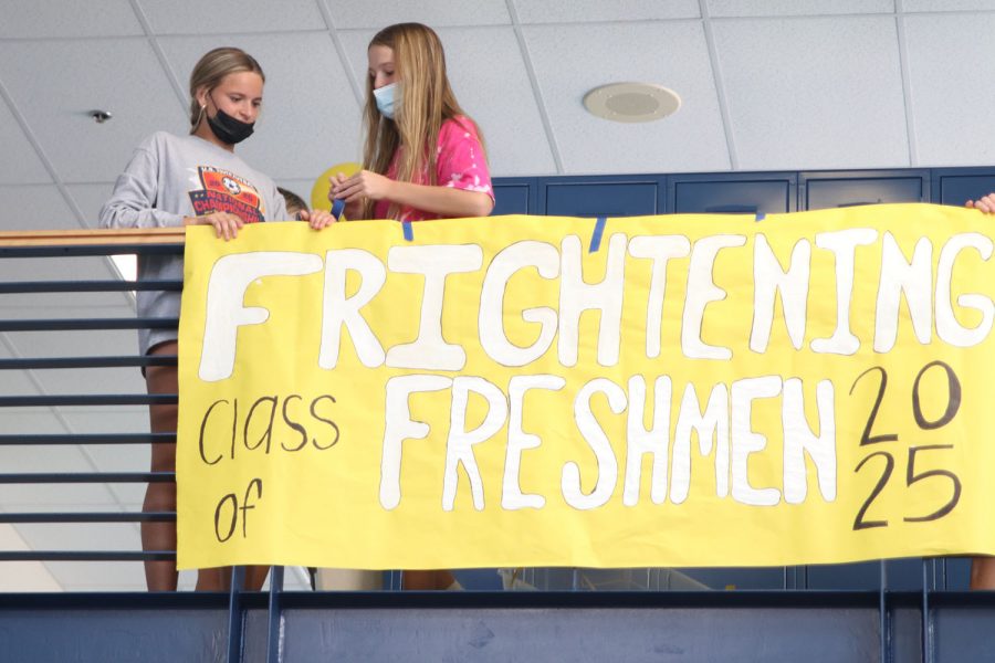 Tape in hand, freshman Addison Long works on hanging a sign as freshman Marissa Hoelting holds it in place. 