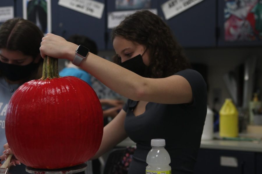 Dipping her paintbrush to get more paint, junior Alex Cobin finishes up painting her pumpkin a bright red.