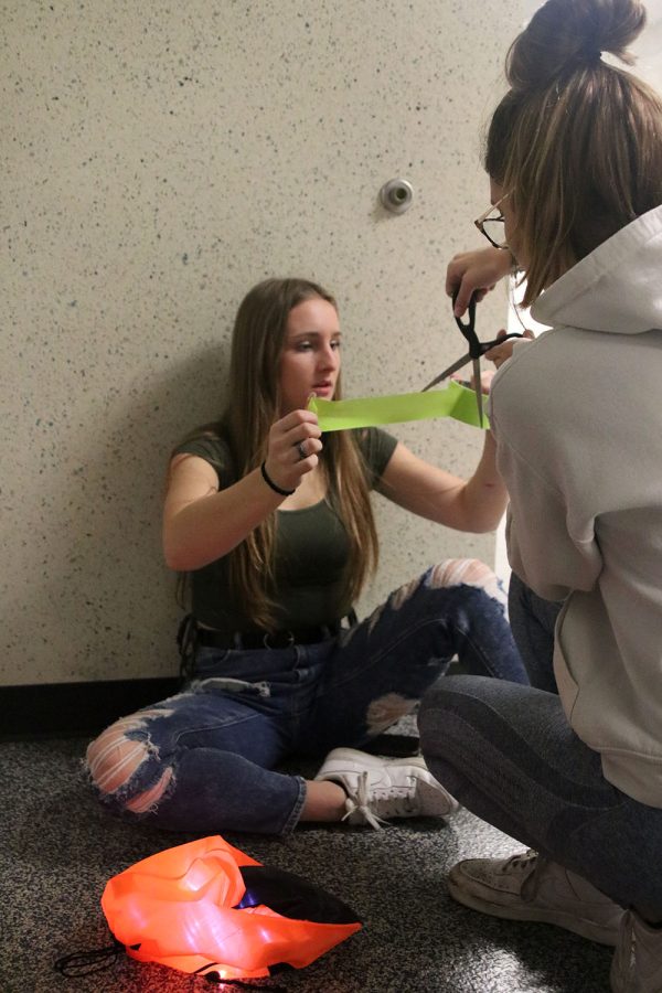Holding a piece of tape, junior Jayda DeWitte helps decorate her seminar door for red ribbon week.