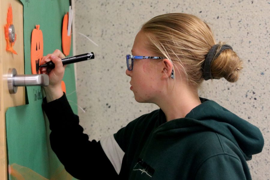 With a black marker in her hand, freshman Laura Hickman finishes drawing the mouth of her pumpkin to fit her Halloween-themed decorated door.