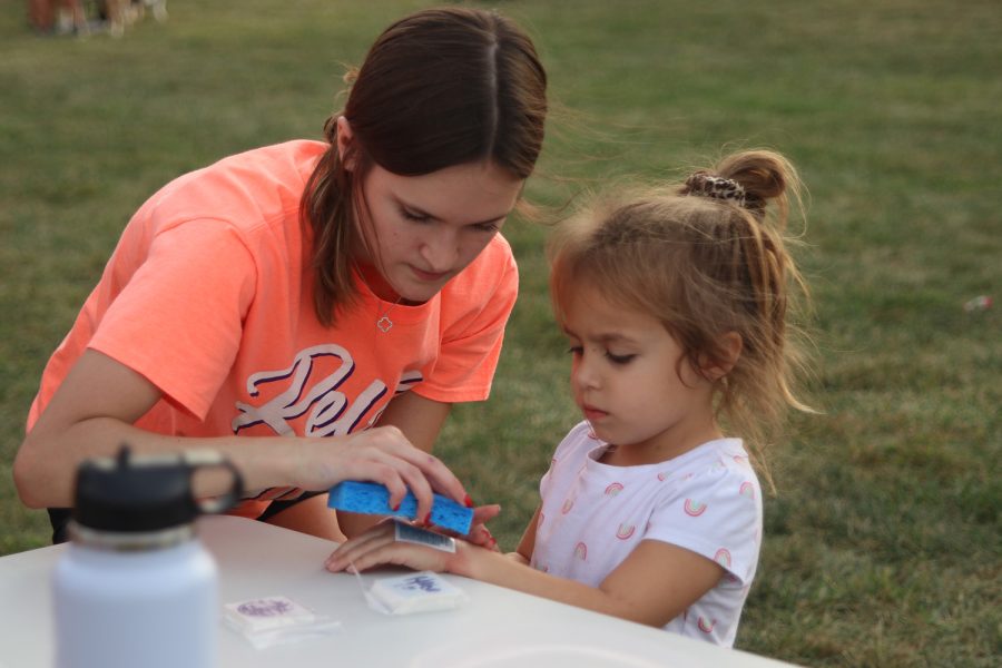 Focused, senior Madison Shaw applies a temporary tattoo onto a child's hand. 
