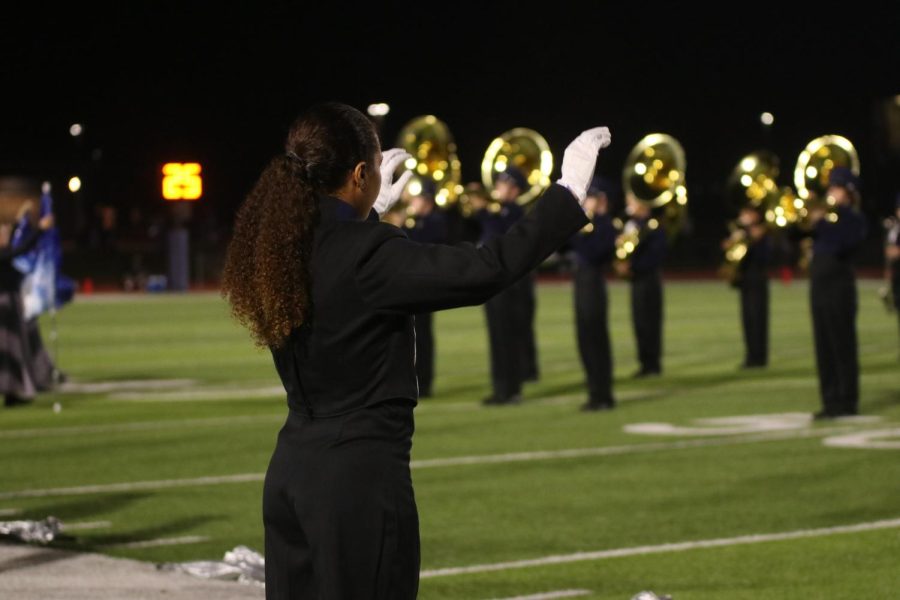 On the sidelines, drum major junior Gabby Delpleash lifts her arms to conduct the band