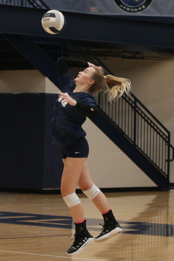 In the air, senior Annabelle Manning serves the ball.