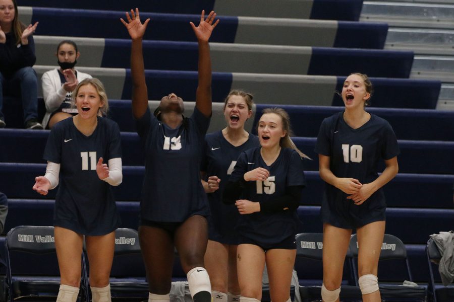 On the sidelines, members of the volleyball team cheer as they score a point.