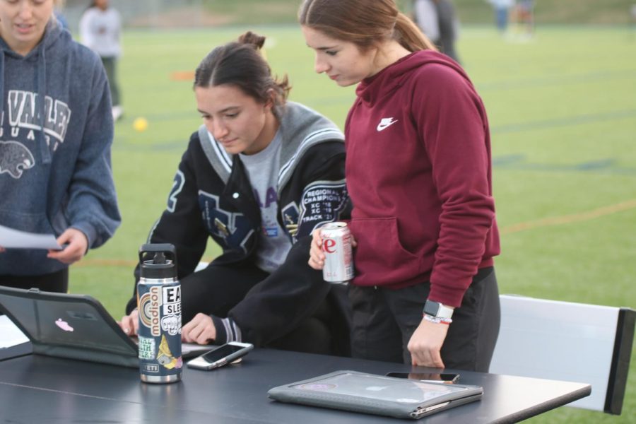 Looking down at the screen, seniors Anna Brazil and Quincy Hubert check participants in. 