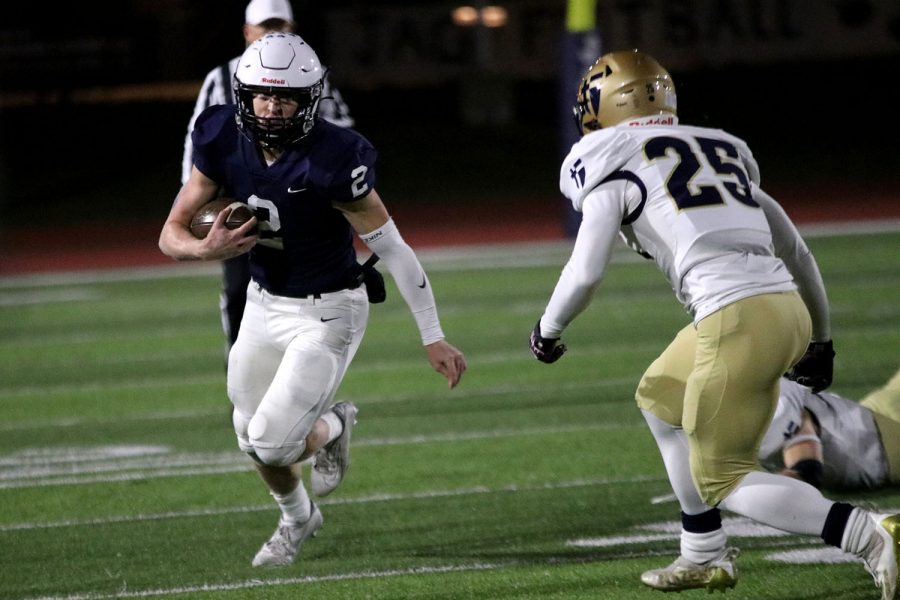 With his opponent in front of him, junior quarterback Hayden Jay carries the ball down the sideline of the football field.