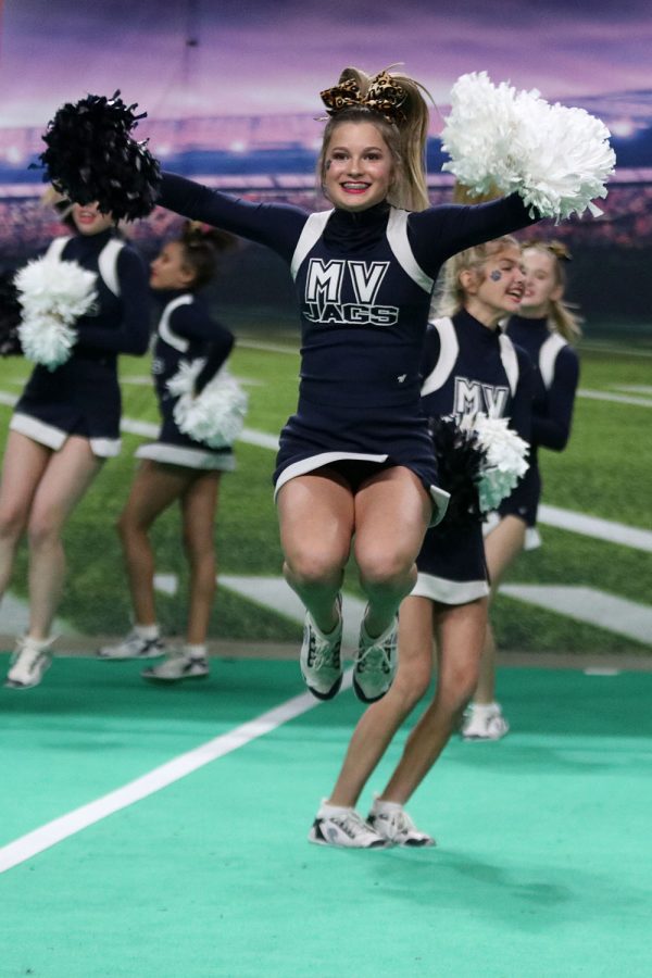 In midair, freshman Joey Nightingale jumps up with her pom poms to her side as the cheer team gets ready to perform their fight song.