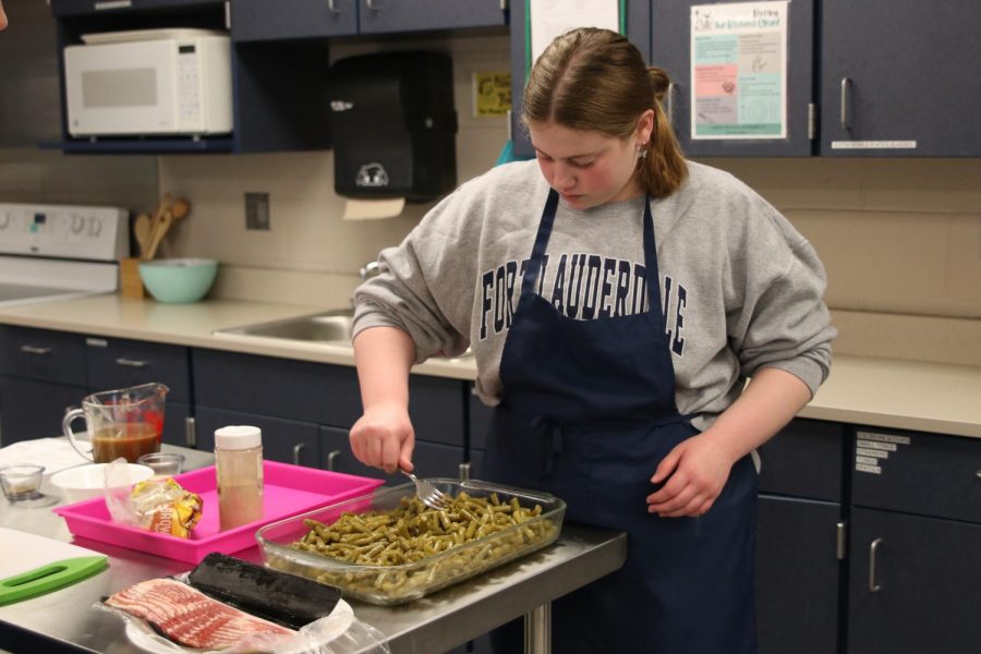 Stirring up green beans, sophomore Molly Bilhimer spreads the casserole out evenly in the pan. 