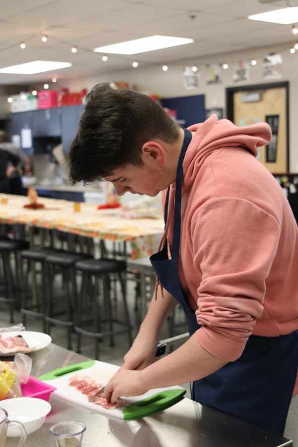 Using a cutting board and knife, junior Devin Sitcler chops up bacon to add to the top of the green bean casserole. 