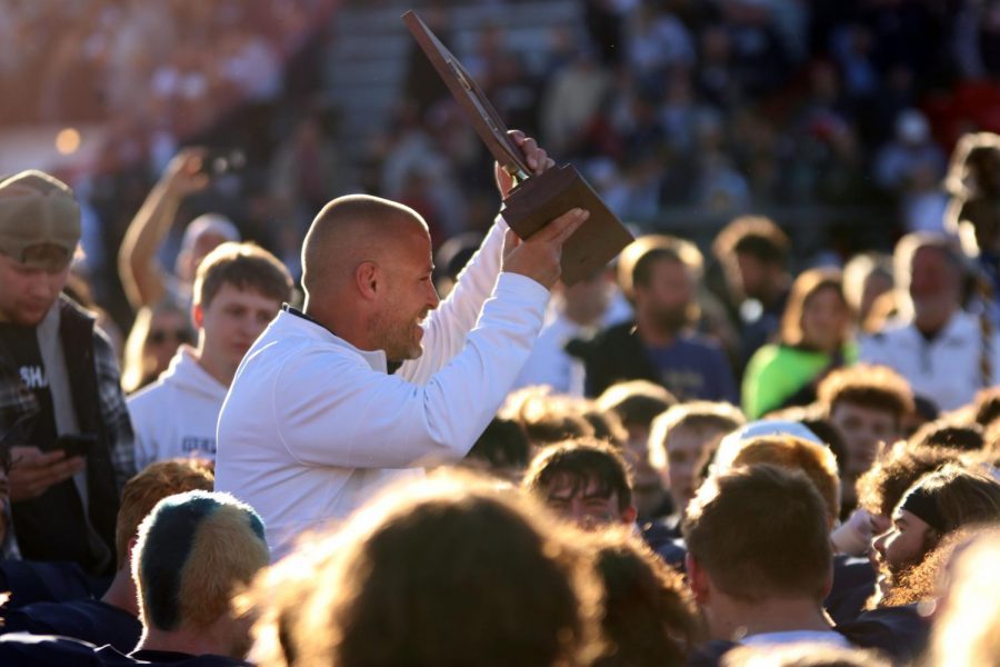 Coach Joel Applebee holds up the state championship trophy for a crowd of family, players, students, and staff.