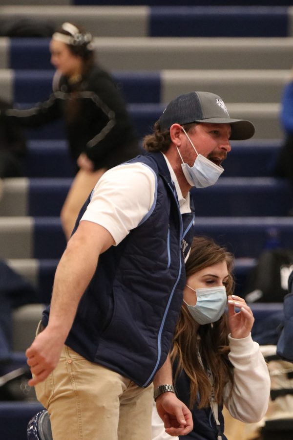 Standing up from his chair, coach Jake Ellis shouts directions at senior Rylee Allen-Atchison as she wrestles on the mat.