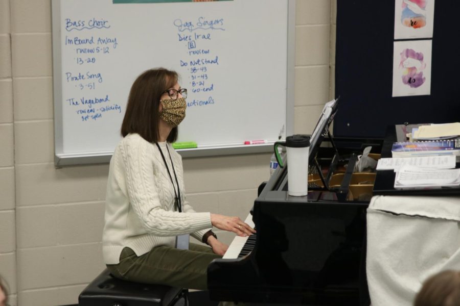 Glancing at her sheet music, accompanist Cindy Rhodes plays the piano to assist the choir students in singing 