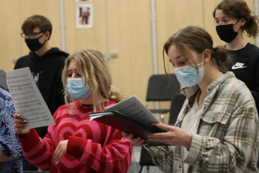 Looking at their sheet music, sophomores Violet Hentges and Grace Cormany practice a choir song.