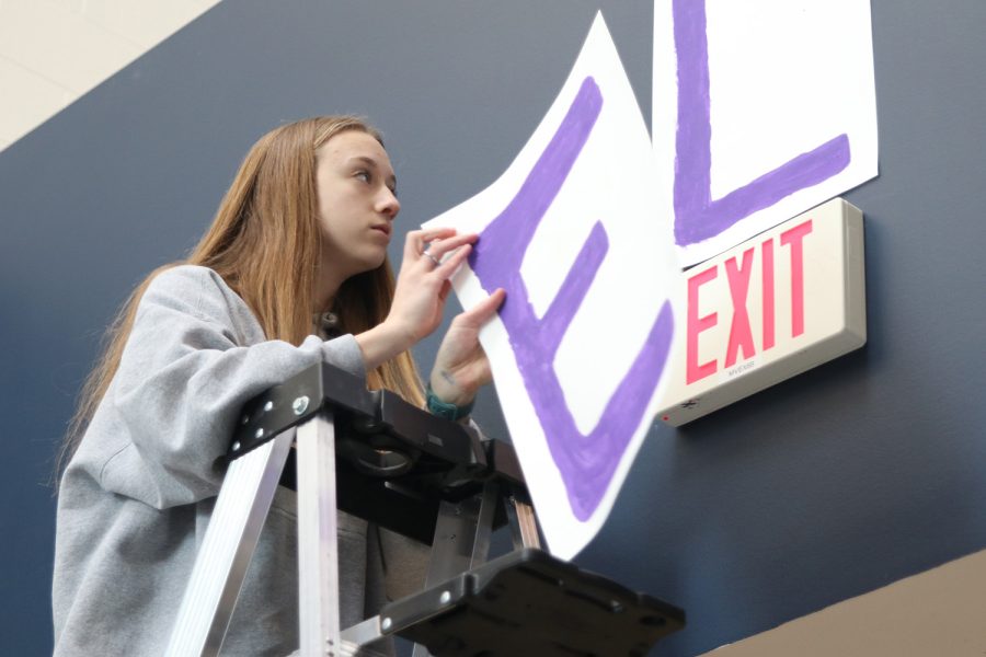 On a ladder, senior Hadley Skinner hangs letters to spell “Relay” Monday, Feb. 21 above the Performing Arts Center doors. 
