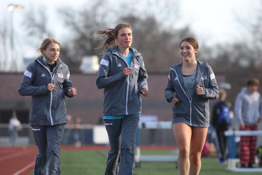 Smiling at one another, seniors Bridget Roy, Logan Pfiester and Anna Brazil run around the inside of the track to warm up for their next race.