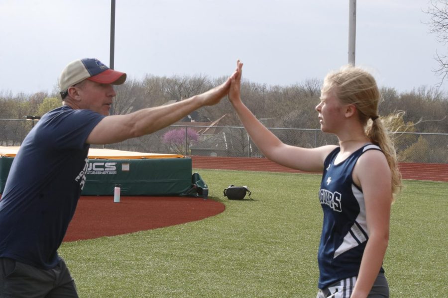 On the sidelines, head track coach Chris McAfee high-fives freshman Sierra Manning to congratulate her on her finish in the 1600 meter run.