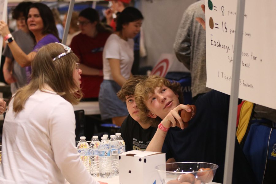 Pointing to the sign hanging above his booth, sophomore Aidan Stroebel explains how to win prizes at his booth.