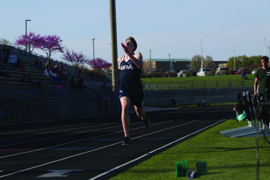 With his arm raised in the air, junior Dylan Miller runs along the track.