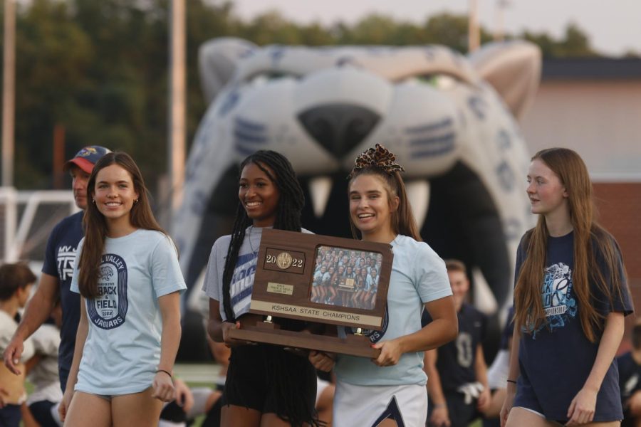 Walking down the football field with tracks state trophy from the 2022 season are Juniors Ava Fleetwood, Makenna Payne, Michelle Marney and Senior Savannah Harvey.