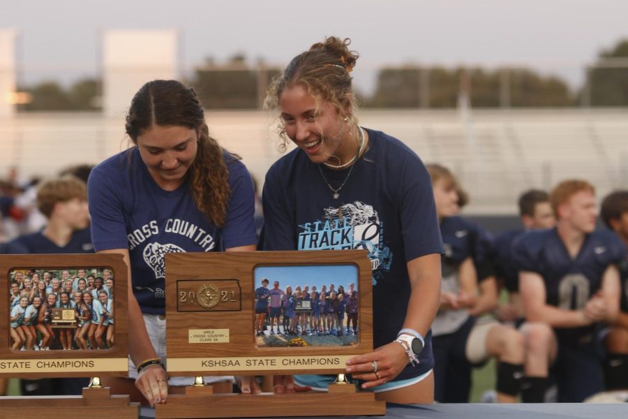 Putting the cross country state trophy on the table are juniors Sarah Anderson and Kynley Verdict.