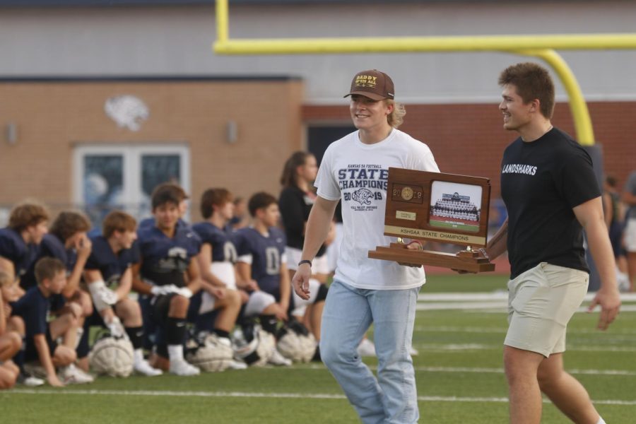Walking across the field with the football state trophy form 2019 are alumnis Grant Frost and Carson Caldwell.