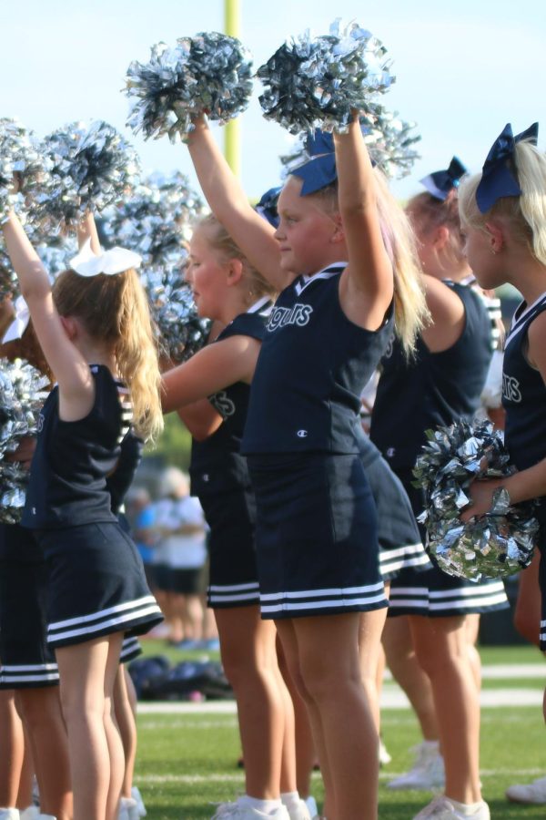 Pom poms in the air, an elementary school cheerleader cheers from the sidelines. 