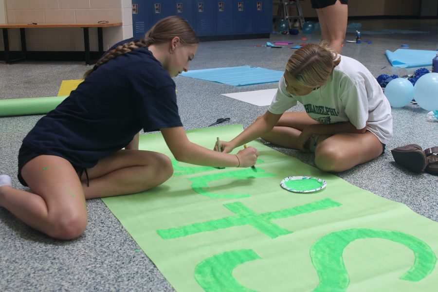 Working together, sophomores Josie Benson and Maggie Wieland paint a poster for their grade. 