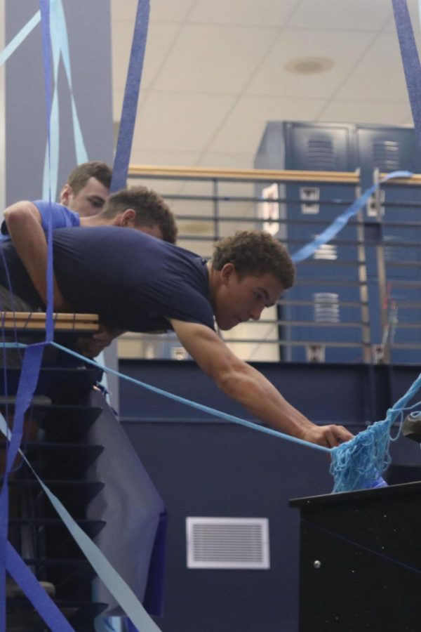 Being held by his friend, senior Luke Shideler reaches out to create a cup tower on the jaguar stand.