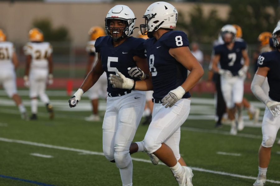 Celebrating the previous play next to junior Truman Griffith, sophomore Jayden Woods smiles big while running to the sidelines. 
