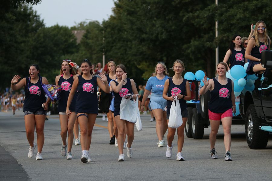 Waving to the crowd, senior Powderpuff players walk alongside the senior class float. 