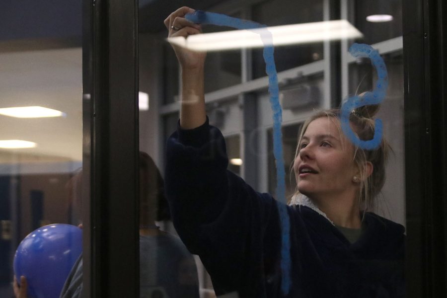 Concentrating on writing on the window, senior Bella Mehner writes out “senior” in blue ink.