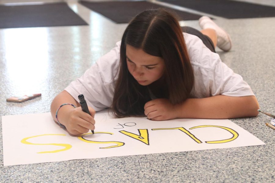 Laying on the floor making a poster, freshman Lily Suman concentrates on coloring the words “class of 2026” in.
