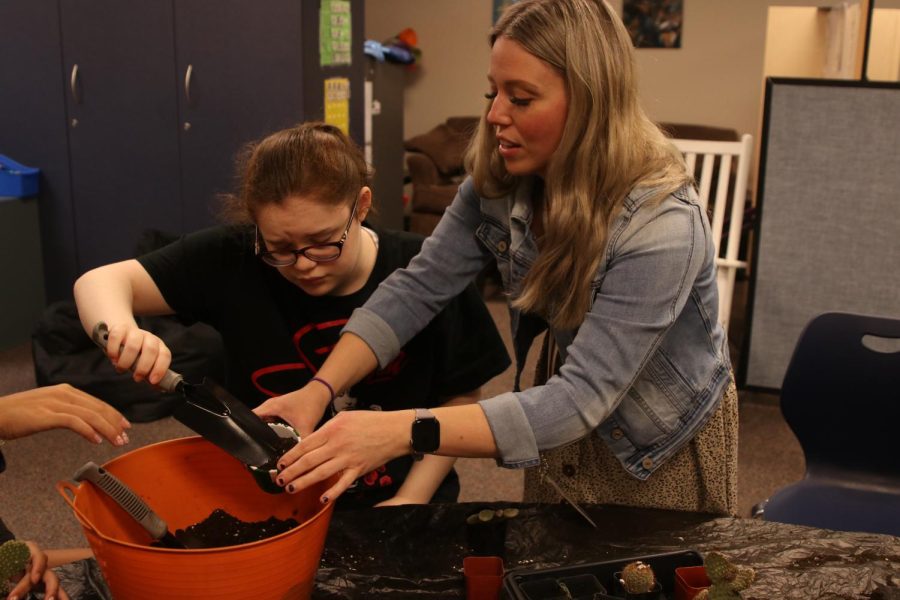Special education teacher Kaila Masters holds a pot as sophomore Robyn Bishop shovels dirt into it