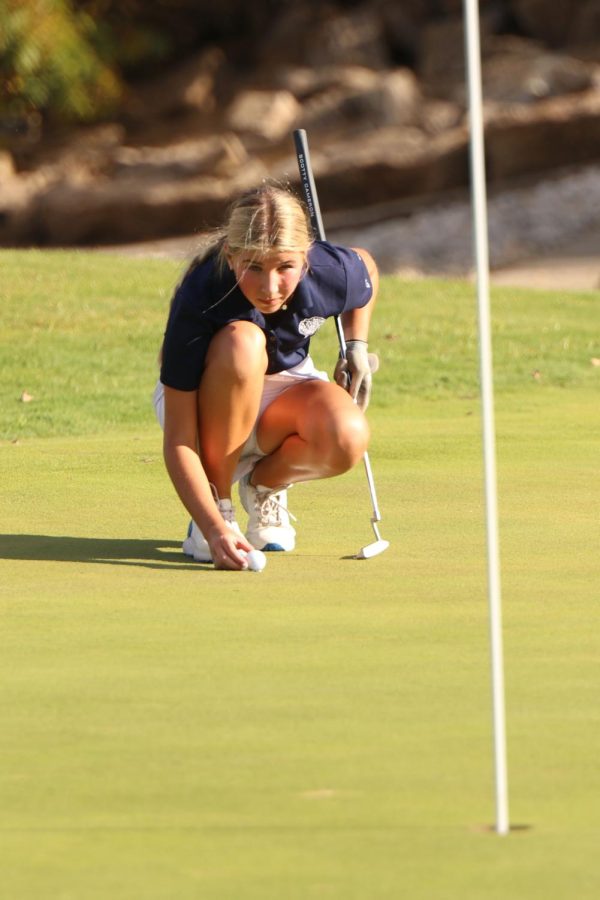 Lining up her shot, freshman Sydney Epperson places her ball on the green. 