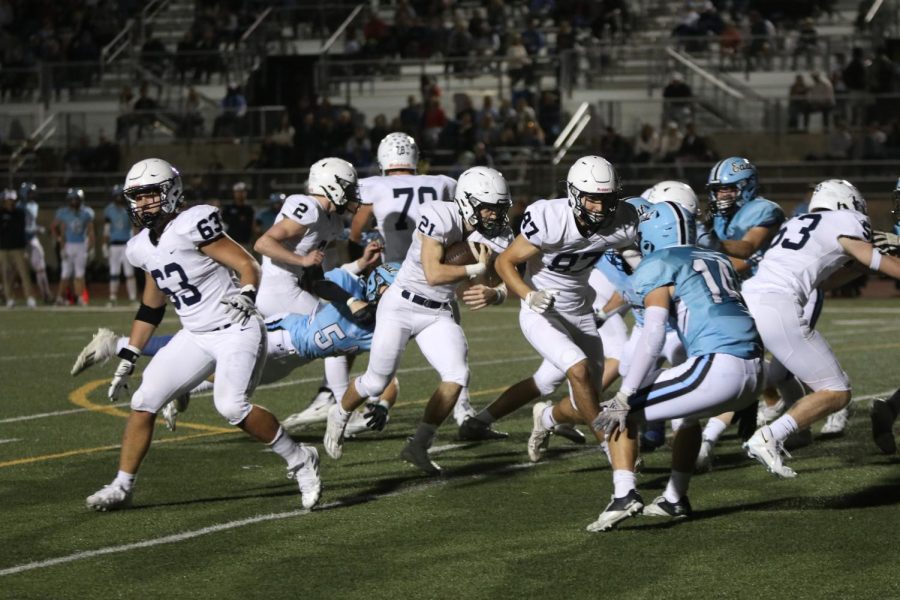 Running toward the end zone, junior Tristan Baker carries the ball through a pack of members from the opposing team. 