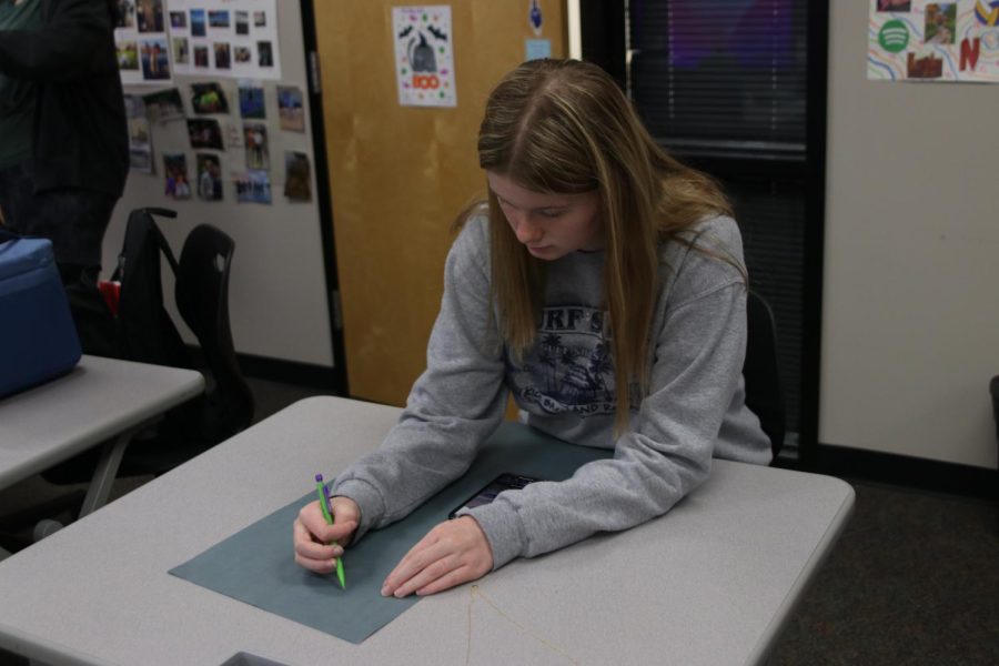 Looking down at her phone and sketching out a person on paper is Junior Jenna Graber on Tuesday, Oct. 26.