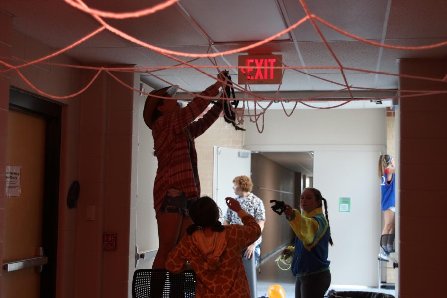 Junior Kate Pfiester hangs up a decorative spider in a spider web.