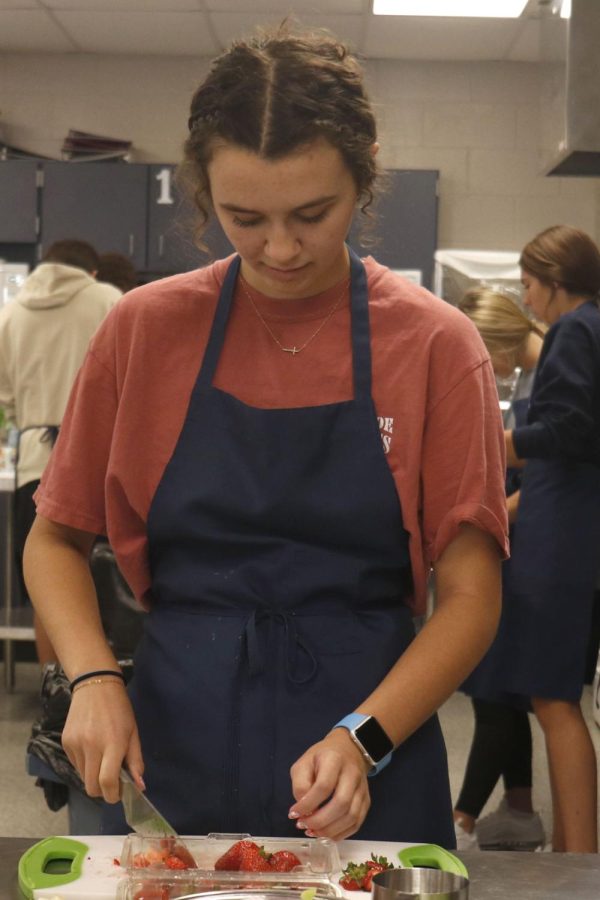 Determined to finish making her food before the class ends, senior Makenna Arnold scrapes the chopped strawberry to the side.