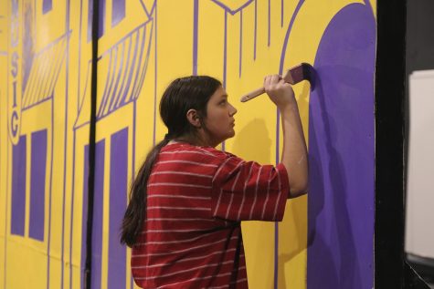 Adding a pop of color, Hayden Rider paints using a cooler toned purple to contrast from the yellow paint on a New York City inspired set Saturday, Oct. 29.