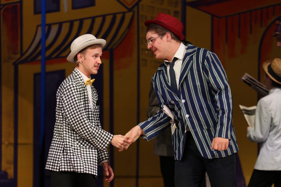 Arms extended, Nathan Detroit, played by senior Carter Harvey, shakes hands with Harry Horse, played by junior Blake Powers. 