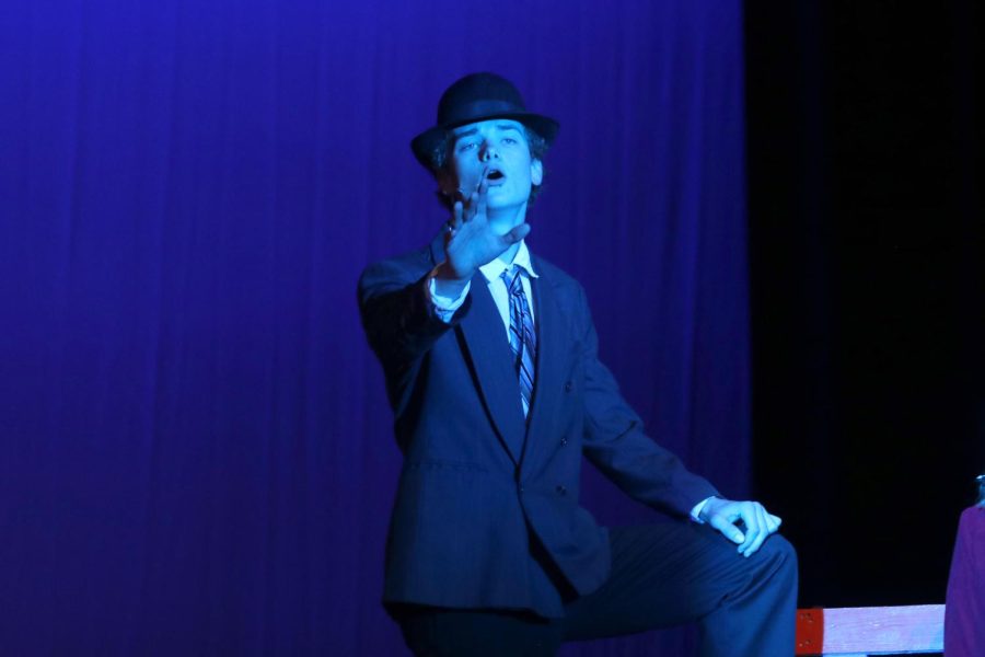 Arm reaching out, senior Finn Cambell sings to the audience while playing the role of Sky Masterson. 
