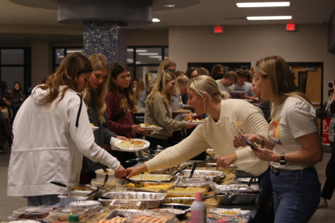 Reaching across the mac and cheese, StuCo advisor Jessica DeWild helps serve students