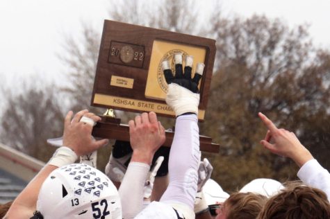 A player holds up a four in front on the state championship trophy.