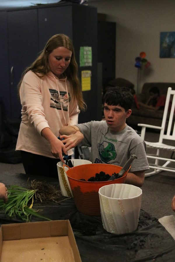 Starting on his first plant, senior Jackson Stutheit shovels dirt into a glitter decorated pot with the helping hand of senior Macee Moore Wednesday, Oct. 26.