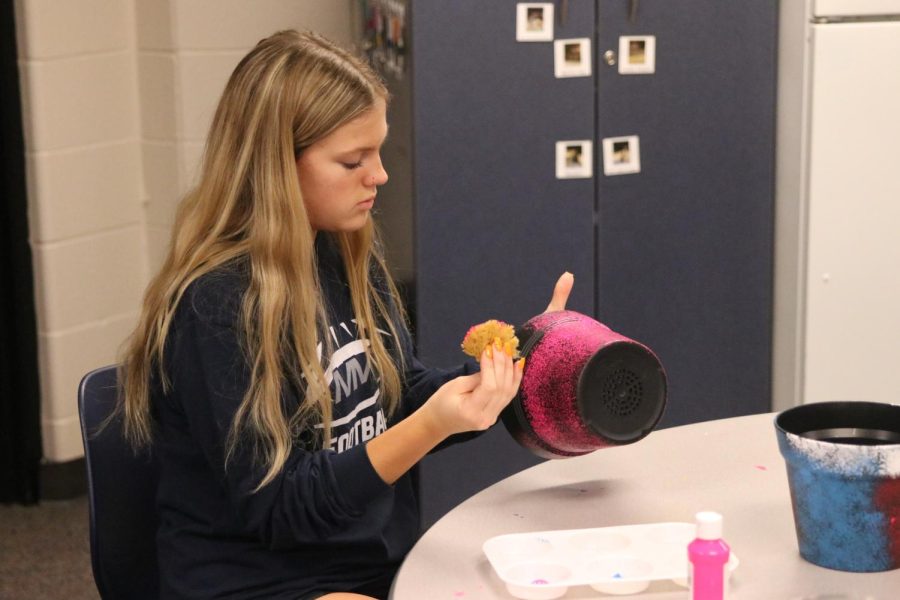 Painting a big pot with a sponge and pink paint, sophomore Reese Hartwich helps decorate the pots Tuesday, Oct. 18. 