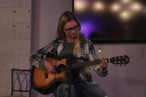 Facing towards the audience Marissa Akehurst plays her guitar.