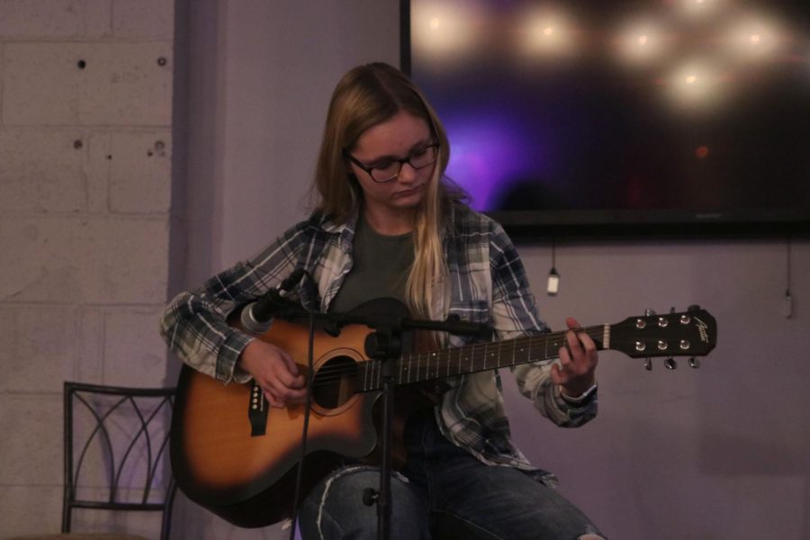 Facing towards the audience Marissa Akehurst plays her guitar.