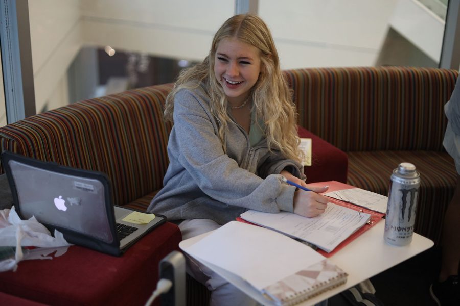 While smiling, junior Violet Hentges does her homework in the local library study room Wednesday, Dec. 14. “The library allows a bigger space for me and my friends that is still a good working environment,” Hentges said. “I like going with friends because having other people around me helps motivate me to get my work done.”